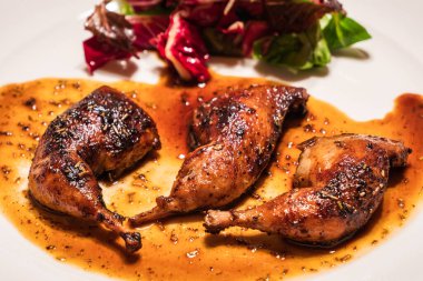 Beyaz bir tabakta Madeira Ju, ot ve salata ile kurutulmuş bıldırcın bacağı.