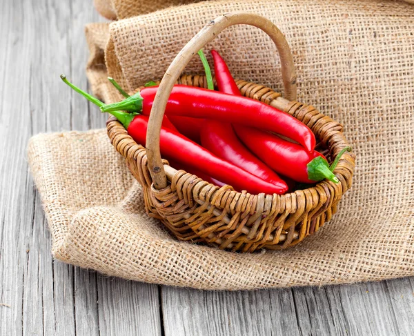 Red chili pepper in a wicker basket with burlap on the wooden ba — Stock Photo, Image