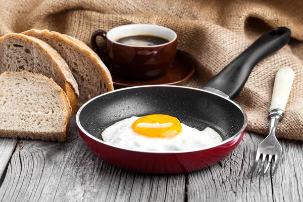 Fried egg in a frying pan, on an old wooden table — Stock Photo, Image