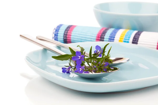Посуда с голубыми цветами лобелии и столовые приборы, на белой спине — стоковое фото