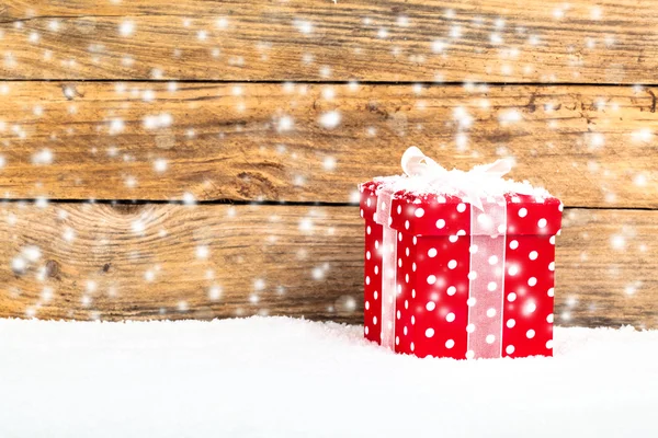 Κόκκινο δώρο για τα Χριστούγεννα σε ξύλινα φόντο με χιόνι — Φωτογραφία Αρχείου