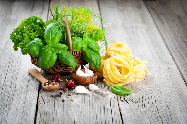 Nido de fettuccine pasta italiana con cesto de mimbre hierbas verdes, en —  Fotos de Stock