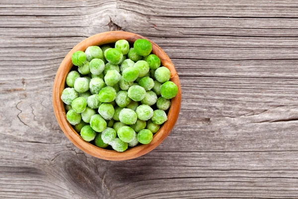 Green peas in wooden bowl on wooden background — Stock Photo, Image