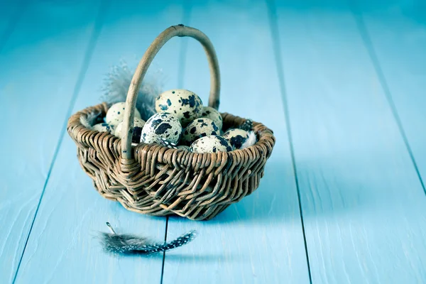 Quail eggs in a wicker basket on blue wooden background — Stock Photo, Image