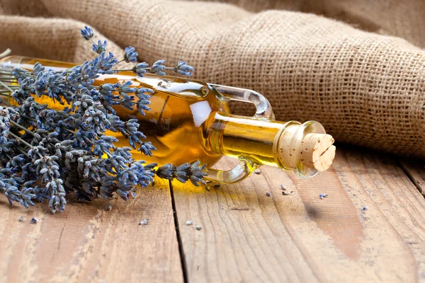 Bottiglia di olio essenziale e fiori di lavanda, su fondo di legno . — Foto Stock