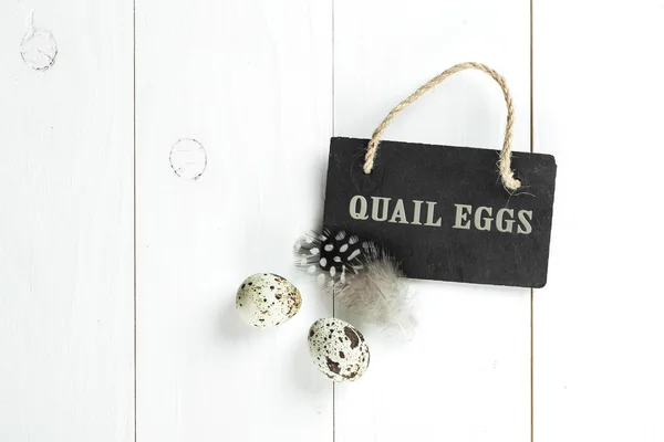 Αυγά ορτυκιού και φτερό με vintage μαυροπίνακα στον λευκό ξύλινα β — Φωτογραφία Αρχείου