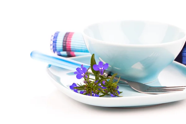 Utensílios de mesa com flores de lobelia azuis e talheres, em umas costas brancas — Fotografia de Stock
