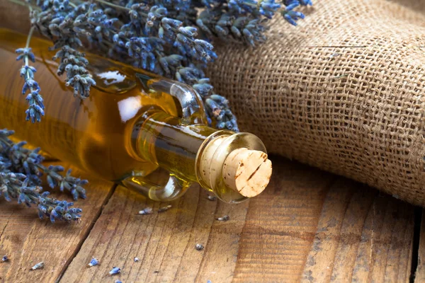 Botella de aceite esencial y flores de lavanda, sobre fondo de madera . — Foto de Stock