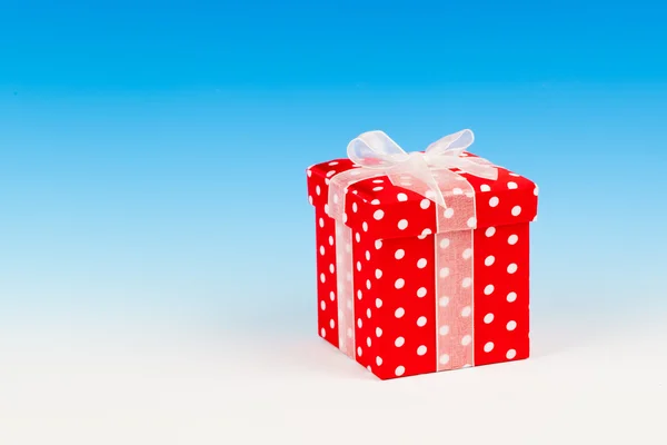 Red gift box, polka dots with bow on blue background — Stock Photo, Image