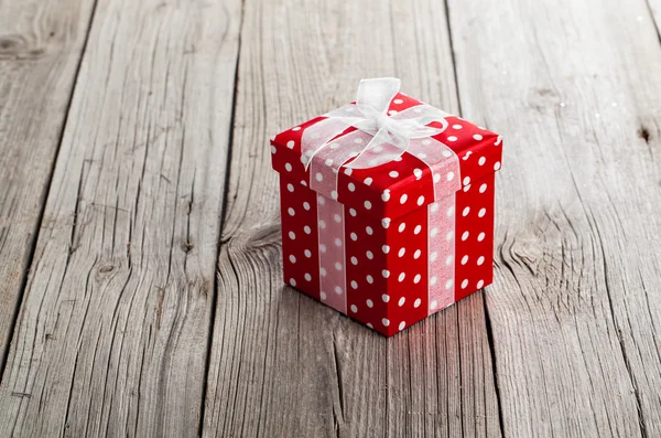 Ahşap zemin üzerinde fiyonklu kırmızı hediye kutusu — Stok fotoğraf