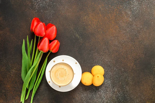 Red tulips and coffee cup on dark table. Top view with copy space