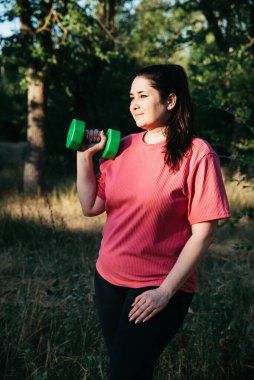 A plus-size woman doing dumbbell exercises outdoors. Outdoor sports. Green dumbbells in the athletes hands. High quality photo
