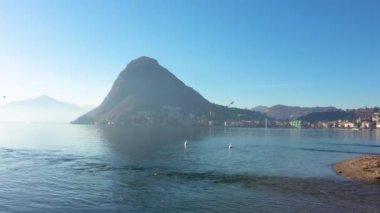 Lugano Gölü 'nün havadan görünüşü. Suda yüzen kuğular ve mavi gökyüzünde uçan martılar. İsviçre 'de İHA ile vur. 
