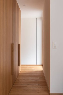 Beyaz duvarları ve ahşap zemini olan modern bir ev. Ahşap dolapları olan bir koridor. İçeride kimse yok.