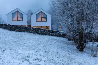 Doğayla, karla ve sisle çevrili geniş pencereli modern beyaz bir ev. Noel havası. İçeride kimse yok..