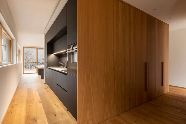 Modern home interior with white walls and a parquet on the floor. Modern black kitchen and large cupboards. Landscape. Nobody inside