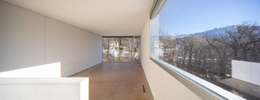 Tek bir aile evinin içi, geniş boş bir alan, doğa manzaralı, pencereler büyük..