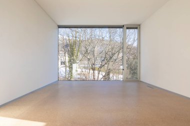 Geniş pencereli, boş bir odanın içi. Duvarlar beyaz.