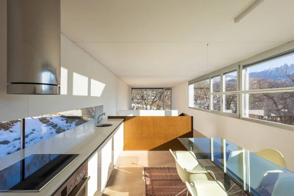 Kitchen with dining room of a cozy and modern apartment. large window with a view on a blue sky mountains to forest.