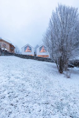 Doğayla, karla ve sisle çevrili geniş pencereli modern beyaz bir ev. Noel havası. İçeride kimse yok..