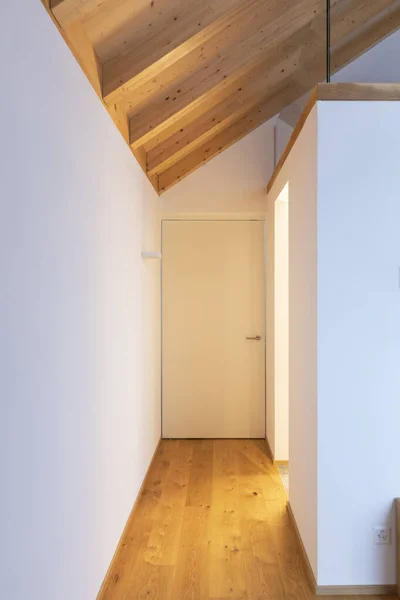 Modern home interior with white walls and hardwood floors. Front view hallway with white door and visible wooden beams. Nobody inside