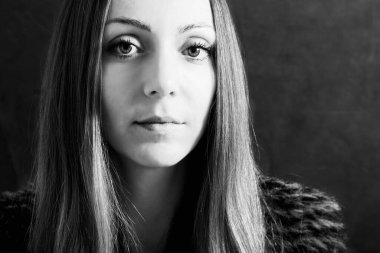 Kürklü kadın stüdyoda karanlık arka planda oturuyor. Siyah beyaz portre