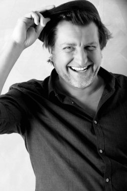 Düğmeleri iliklenmemiş gömlekli 50 yaşında bir adamın portresi. O, şapkasını tutarken güler. Balkon ve beyaz fotoğraf