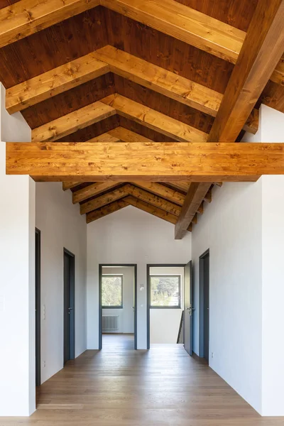 Front view hallway with exposed wood beams and open doors to empty rooms, paquet floor. Nobody inside.