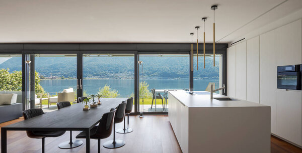 Интерьер современной квартиры, со столовой и открытой кухней. Вид спереди. Во время еды из окон открывается потрясающий вид на озеро. Никто внутри, стол на шестом..