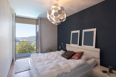 Büyük beyaz yataklı şık bir yatak odası ve göl manzaralı bir balkon. İçeride kimse yok.. 