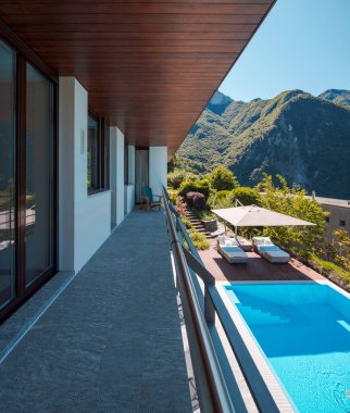 Kaya zemin ve ahşap tavanlı villanın balkonunda. Aşağıda yüzmek için mükemmel bir havuz var. İsviçre 'nin yeşil dağlarının manzarası. İçeride kimse yok.