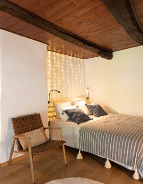 Büyük, çift kişilik yataklı, üzerinde bir sürü ışık olan samimi bir yatak odası. Eski bir sandalye atmosferi daha romantik yapar. İçeride kimse yok.