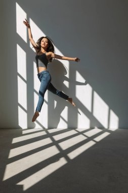 Asyalı dansçı kız, boş bir binanın camından içeri giren güneşin aydınlattığı akrobatik bir atlayış yapıyor. izole