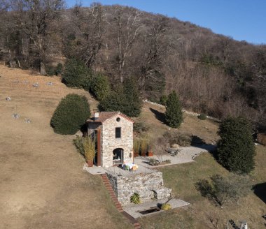 Doğayla çevrili, önünde yaşlı bir zeytin ağacı olan çok küçük bir ev. Koyu mavi gökyüzü ile güneşli bir gün. Sonbahar olmasına rağmen, çimenler yeşildir. Hava görüntüsü, dronla çekilmiş.