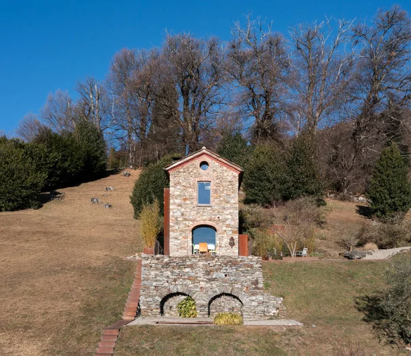 Doğayla çevrili, önünde yaşlı bir zeytin ağacı olan çok küçük bir ev. Koyu mavi gökyüzü ile güneşli bir gün. Sonbahar olmasına rağmen, çimenler yeşildir. Hava görüntüsü, dronla çekilmiş.
