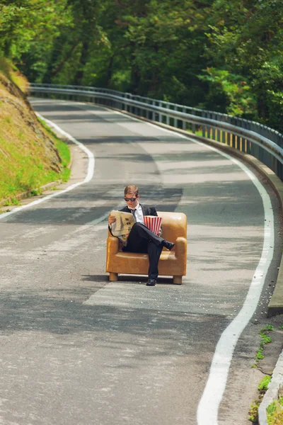 Hombre de negocios sentado en un sillón en medio de la carretera — Foto de Stock
