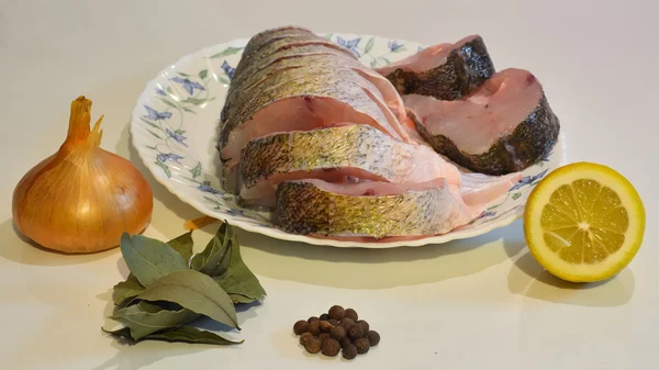 Balık bir plaka üzerinde soğan, dilimlenmiş biber, defne yaprağı, limon