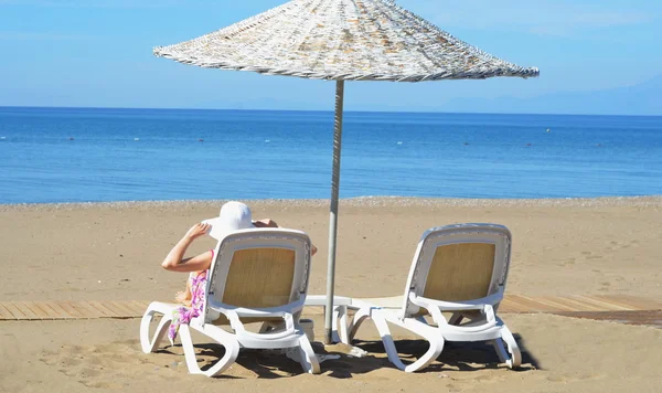 Kvinna, bakifrån på solstol på sandstrand med blå himmel — Stockfoto