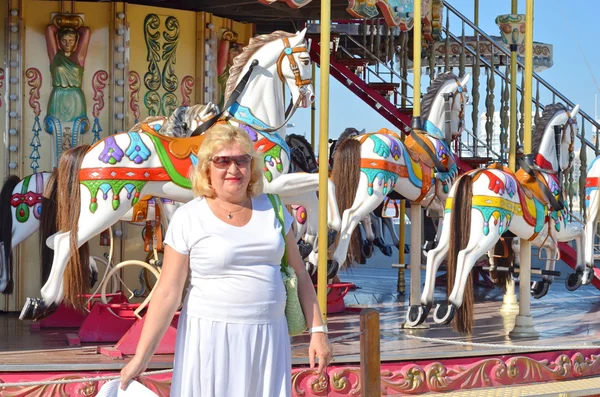 Uśmiechający się starszy kobiety stojącej w pobliżu karuzela z systemem koni — Zdjęcie stockowe