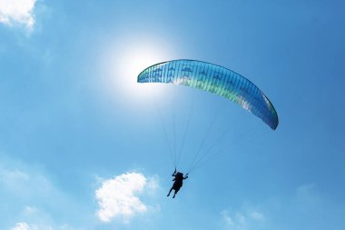 Mavi Paraglider güneşli bir günde bulutlarla gökyüzüne uçuyor.