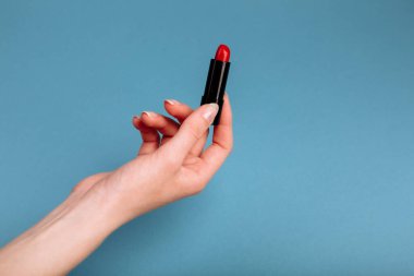 Kadın eli kırmızı ruj alıyor. Mavi arkaplanda izole edilmiş