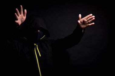 Maskeli hırsız siyah arka planda izole edilmiş kollarıyla seni korkutmaya çalışıyor.