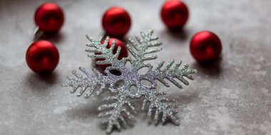 Gri bir arka planda Noel süslemeleri. Odaklanmamış bordo Noel baloları, Noel oyuncakları ve taş süslemelerle çevrili gümüş bir kar tanesi. Üst görünüm.