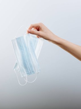 Bir kadın eli, beyaz arka planda izole edilmiş tıbbi bir maske tutuyor..