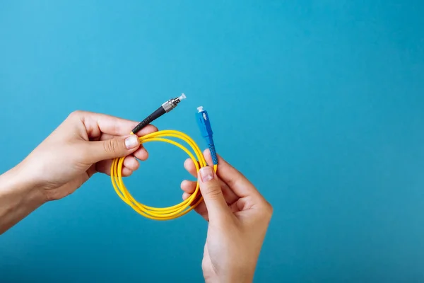 Las manos de las mujeres sostienen SC y FC conector cable de conexión de fibra óptica monomodo sobre fondo azul — Foto de Stock