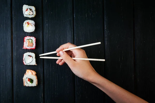 女性的手拿着筷子和中国筷子一起吃寿司卷 躺在一块黑色木板上从上面看 — 图库照片