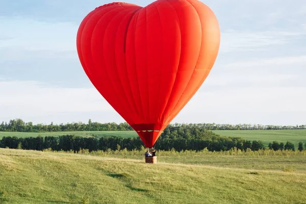 Balon na gorące powietrze w kształcie serca ląduje na zielonym polu — Zdjęcie stockowe