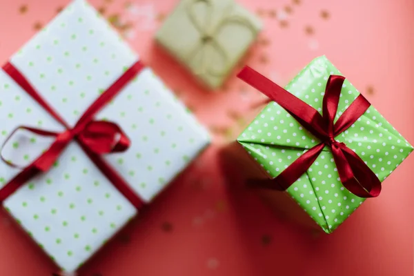 Kleurrijke getextureerde geschenkdozen met lintbogen omgeven door sterren en sneeuwvlokken op koraalachtergrond, van bovenaf. Selectieve focus — Stockfoto