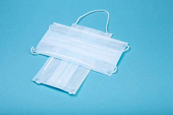 Mavi arka planda, COVID-19 'dan korunmak için iki beyaz cerrahi maskeden yapılan beyaz haç sembolü.