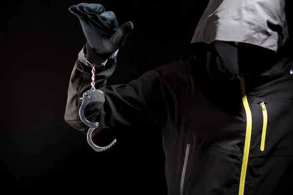 Крупный план рук грабителя в черных перчатках с наручниками на черном фоне — стоковое фото